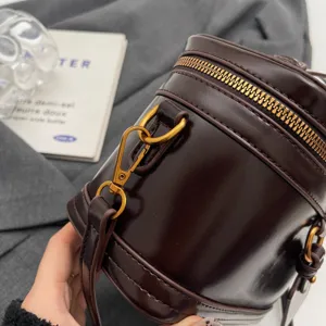Vue détaillée du sac à main cylindrique marron foncé avec fermeture éclair dorée.