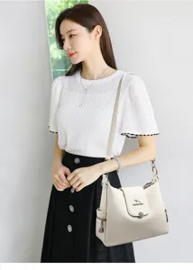 Dettaglio di una elegante borsa a tracolla beige con serratura e scomparti multipli.