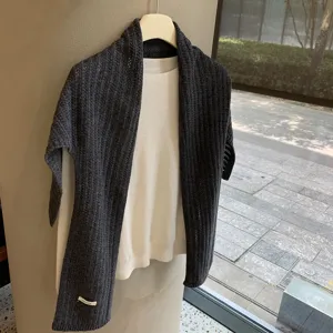 Chal de punto gris oscuro con jersey blanco, detalle de textura en primer plano cerca de la ventana.