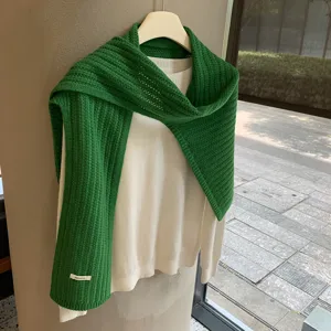 Vista detallada de la bufanda de lana verde y el jersey blanco superpuestos con estilo.