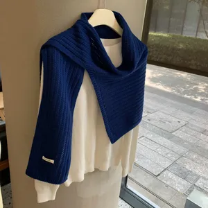 Detalle de primer plano de una bufanda chal de lana de punto azul marino sobre suéter blanco.