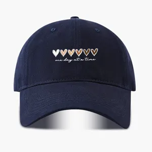 Nahaufnahme der dunkelblauen Baseballkappe mit gestickten Herzen und inspirierendem Text.