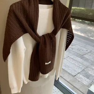 Bufanda chal de lana tejida marrón sobre jersey blanco, vista de detalle de la textura.