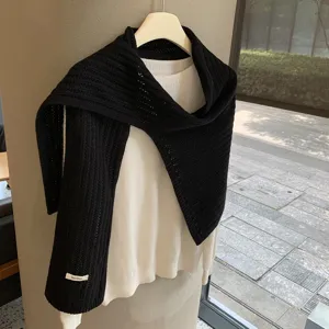 Primer plano detallado de bufanda de punto negro combinada con jersey blanco en percha.