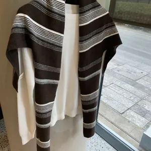 Nahaufnahme eines gemütlichen gestreiften Strickschals über einem weißen Pullover im Innenbereich.