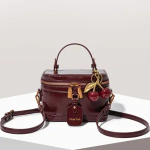 Élégant sac vanity femme en cuir vernis avec poignée, charm cerise et bandoulière chic.