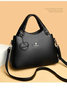 Détail de sac à main en cuir noir avec pendentif cœur et logo métal, sac porté épaule élégant.