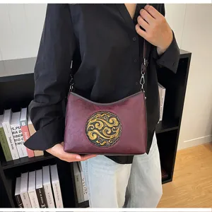 Vue détaillée d'un sac à bandoulière en cuir véritable style chinois avec médaillon doré.