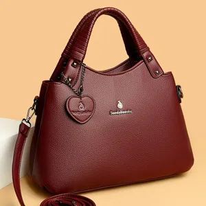 Détail de sac à main rouge vin pour femme avec logo en métal et charm cœur en cuir texturé.