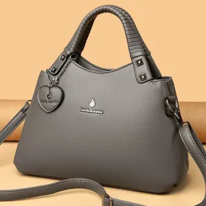 Détail de sac à main en cuir gris avec poignée tressée, logo en métal et bandoulière élégante.