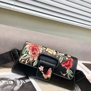 Détail de broderie du sac à bandoulière noir vintage avec motifs floraux et large sangle.