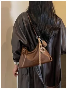 Détail de sac bandoulière en cuir marron, sac hobo élégant avec lanière tressée et charm.