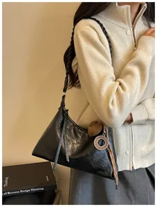 Vue détaillée d'un sac porté épaule noir avec bandoulière tressée et pendentif.