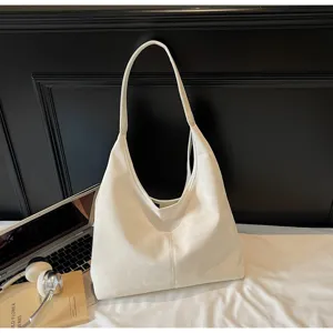 Vue détaillée d'un grand sac hobo blanc élégant placé sur un lit avec des accessoires.