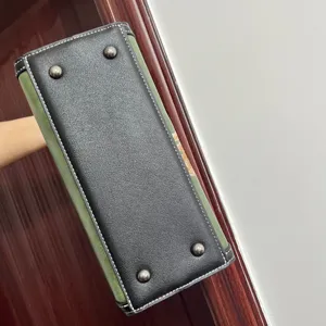 Handbag bottom detail showing black leather base with metal rivets and green side panel.