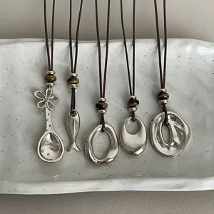 Close-up detail of multi-style pendant necklaces with tiger eye beads on white ceramic tray.