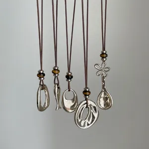 Closeup of retro long necklaces featuring silver pendants like fish, spoon, and tiger's eye beads.