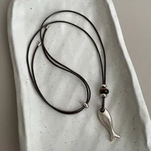 Detailed shot of the metal fish pendant and tiger eye stone bead on the necklace cord.