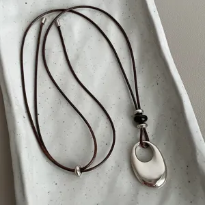 Detailed view of the irregular oval spoon pendant necklace with brown cord and black beads.