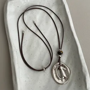 Detail view of irregular oval metal pendant necklace with leather cord and tiger eye beads.