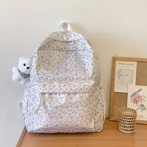 Gedetailleerd overzicht van roze bloemige schoolrugzak met schattige witte berenpluche hanger in kamer.