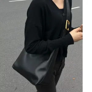 Detail shot of a black shoulder bucket bag with gold square buckle strap, casual street style.