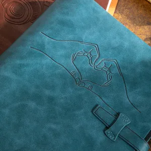Blue faux leather photo album cover detail with debossed heart hands design and leather strap.