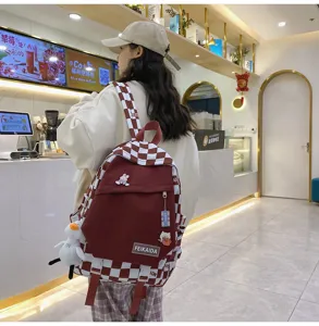 Vista dettagliata di uno zaino scolastico a quadri bordeaux alla moda con simpatici ciondoli.