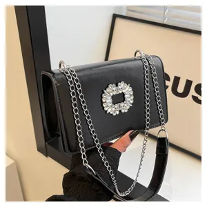 Detail shot of black patent leather small square bag with rhinestone buckle and chain strap.