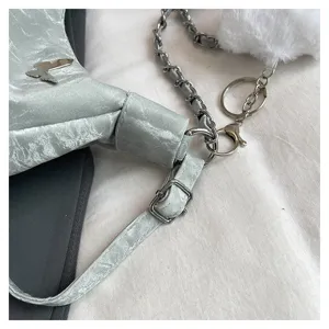 Detailed shot of silver crinkled shoulder bag with metal butterfly and fluffy ball keychain.