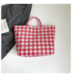 Detailed view of red and white checkered tote bag with blazer and book prop on surface