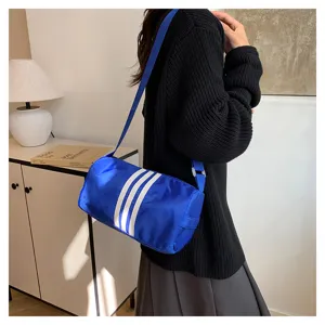 Detailed shot of a blue cylindrical nylon shoulder bag featuring white 3-stripe design.