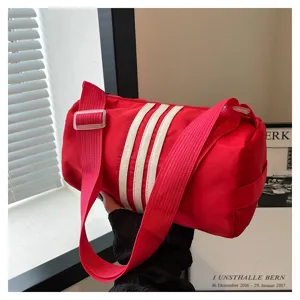 Red nylon cylindrical shoulder bag detail, casual pillow duffel with white stripe accents.