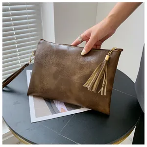 Gros plan détaillé du sac clutch en cuir marron rétro avec texture unique et pompon chic.