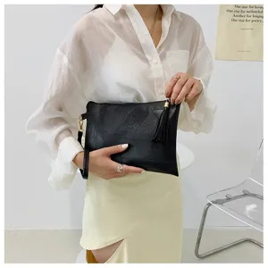 Sac pochette noir pour femme avec texture rétro et pompon, bracelet élégant au poignet.