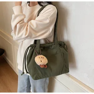 Close-up of dark green corduroy tote bag showing textured fabric, drawstring, and cute pendant.