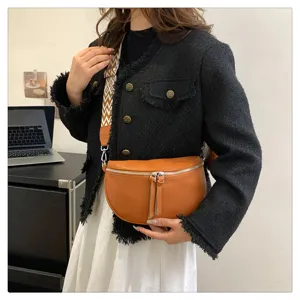 Stylish brown half-moon crossbody saddle bag with wide patterned strap and dual tassel zippers.