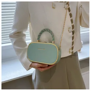 Gros plan du sac à main rigide vert avec chaîne dorée et poignée tordue élégante.