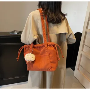 Detail view of the orange corduroy tote bag featuring a drawstring closure and cute plush charm.