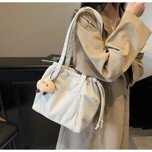 Detail view of white corduroy shoulder bag with drawstring closure and cute plush charm.