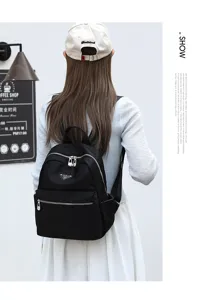 Vue détaillée du sac à dos en nylon noir avec poche avant zippée et logo métallique élégant.