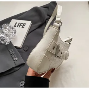 Gros plan de détail d'un sac bandoulière blanc élégant à motif crocodile et boucle métallique.