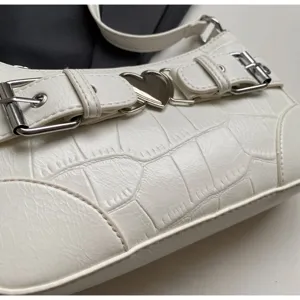 Détail de sac porté épaule croco blanc, chic avec boucles argentées et pendentif cœur charmant.