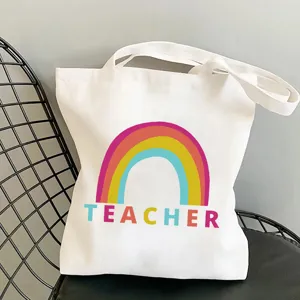 White canvas tote bag featuring colorful rainbow and teacher print for daily shopping use.