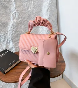 Pink PU leather crossbody bag with heart clasp, scrunchie handle and mini coin pouch detail.
