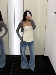 Schlankes geripptes weißes trägerloses Top kombiniert mit grauem Cardigan und Jeans.