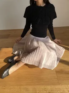 Detailansicht des Damen Plissee Tüll Rock kombiniert mit schwarzem Stricktop flachen Schuhen.