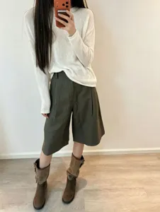Detail view of a casual long sleeve knit top paired with shorts and boots in a clean room.