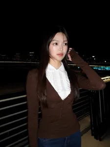 Close up detail of layered brown cardigan with white collar shirt worn by model at night.