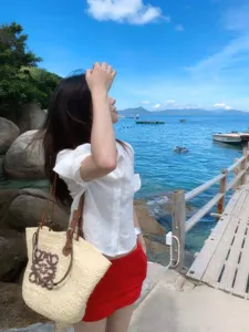 Detailaufnahme von Urlaubs-weißem Hemd und roten Shorts mit Korbtasche am Meer.